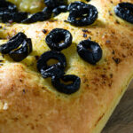 Een vierkante focaccia met groene kruiden en olijven